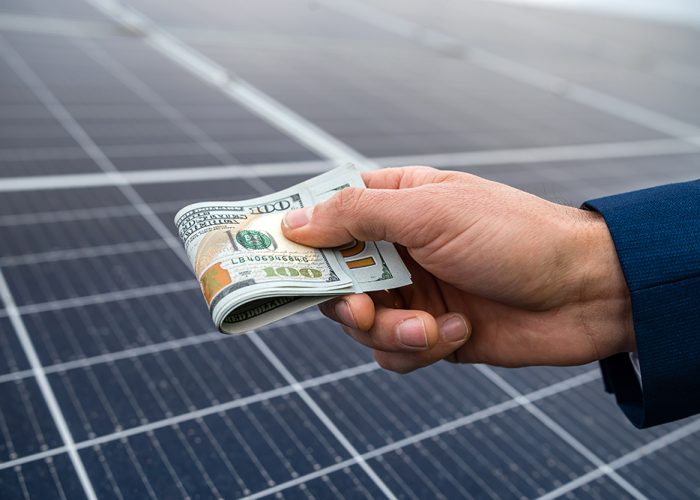 handsome male hands holding dollars to pay for working with solar panels. Green electricity and dollars concept